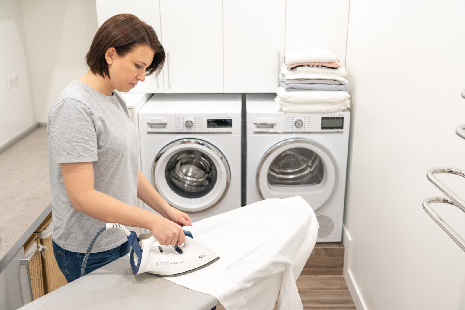 Woman ironing white shirt on board in laundry room with washing machine