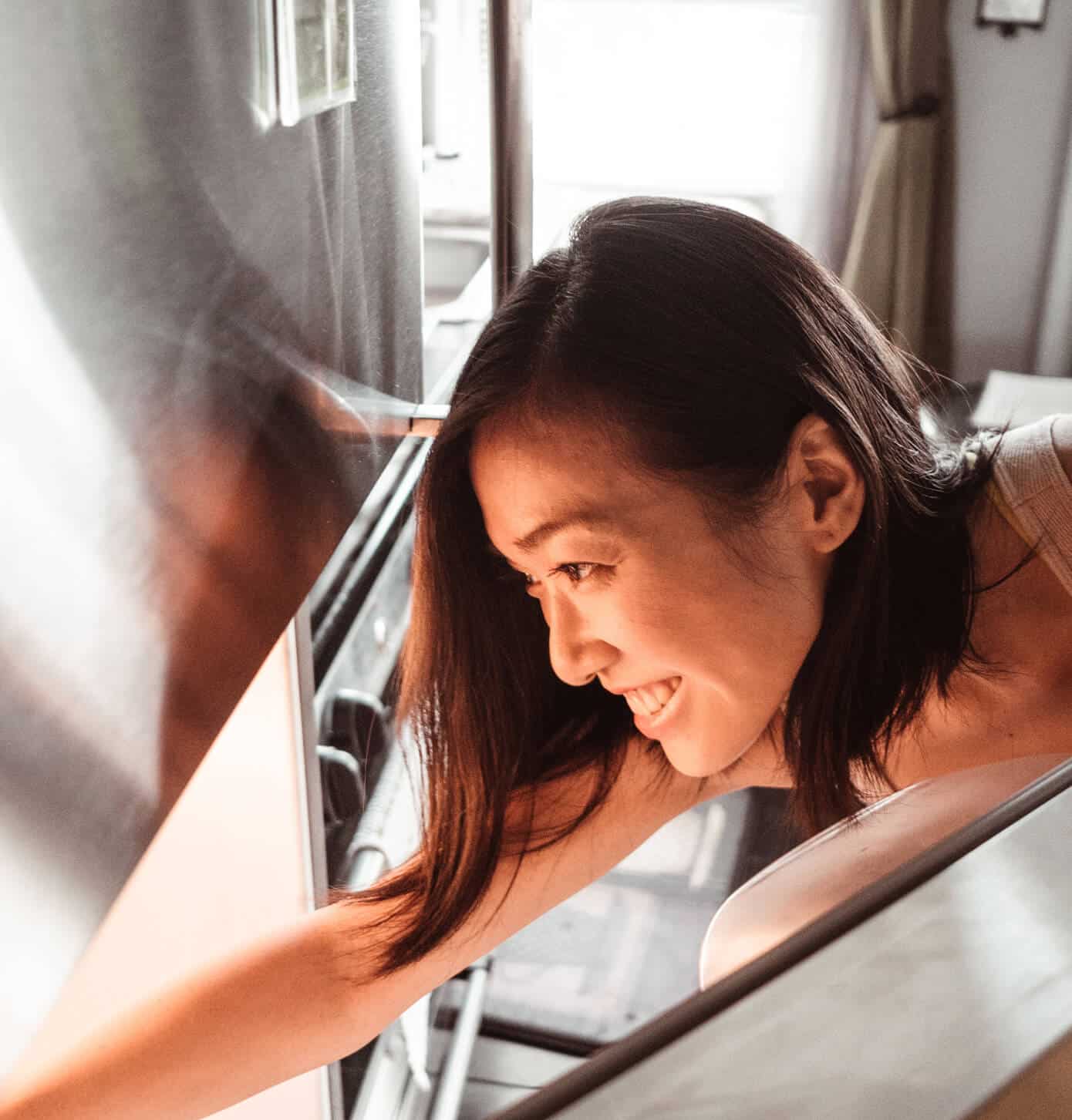 A happy woman smiles as she reaches into her refrigerator after Landers refrigerator service in Baltimore, MD.