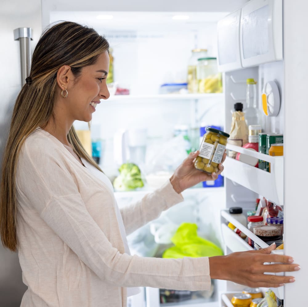 A woman stands at her refrigerator smiling because of reliable Howard County refrigerator repair.