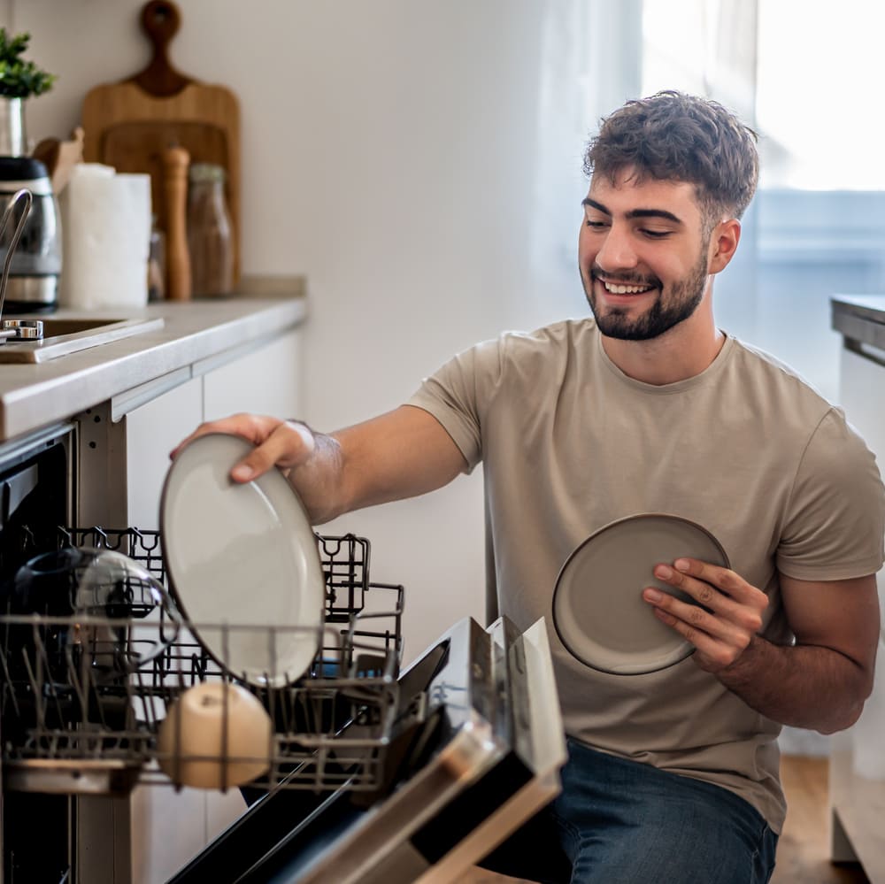 A man happily loads dishes into his dishwasher after Howard County dishwasher repair from Landers Appliance.
