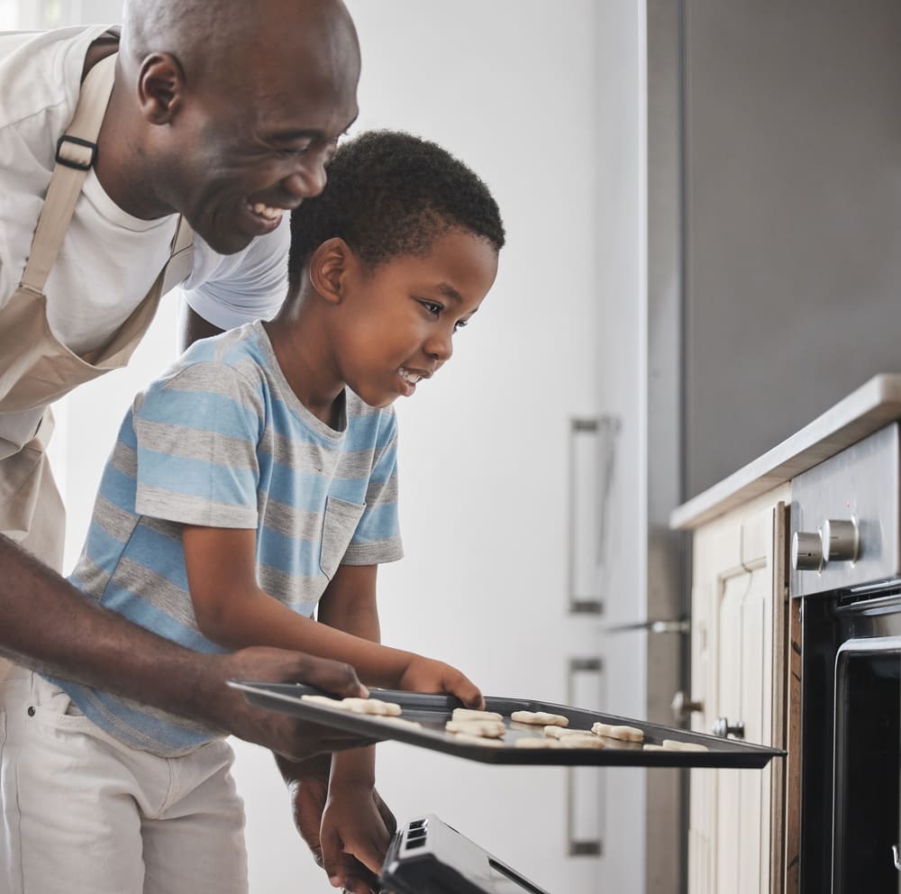 A father and son put cookies in the oven after Howard County oven repair from Landers Appliance.