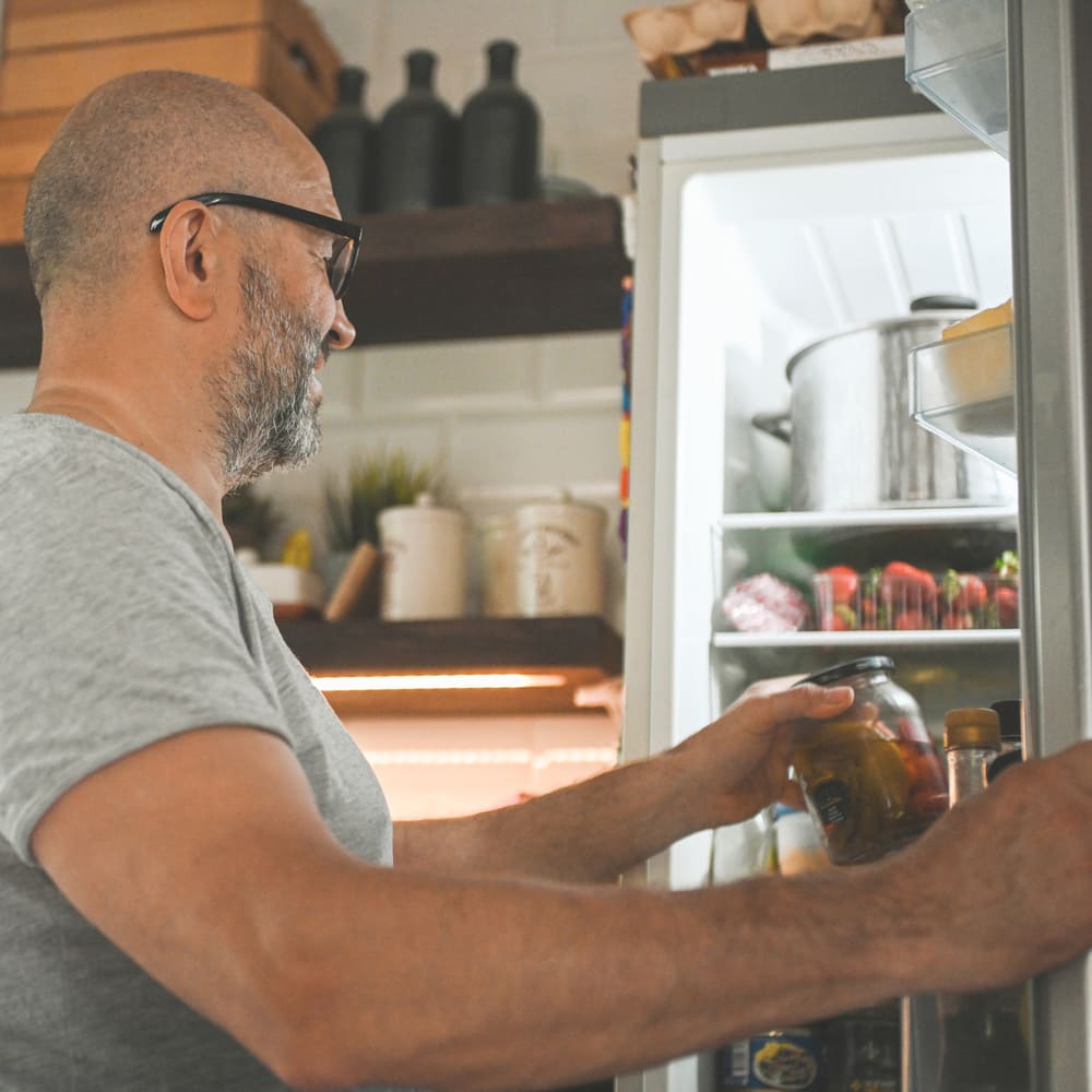 A man smiles as he prepares dinner after reliable refrigerator repair from the Landers Montgomery County crew.